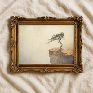Puede incluir: Una impresión enmarcada que presenta un árbol solitario al borde de un acantilado, con un fondo brumoso. El marco dorado y ornamentado añade un toque vintage al arte del paisaje. La silueta del árbol es el punto focal.