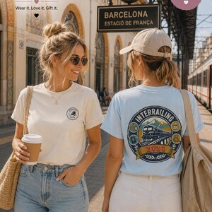 May include: A cream-colored t-shirt with a small circular Europe 2026 logo on the chest and a light blue t-shirt with a large circular Interrailing 2026 graphic on the back featuring a train, mountains, and travel icons.