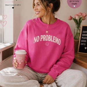 May include: A woman wearing a bright pink sweatshirt with the words "NO PROBLEMO" in white. She is holding a pink coffee cup that says "COFFEE FUELS GOOD DAYS". The image also includes the text "Boffy Boutique" and "your new go-to cosy staple".