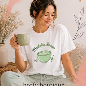 May include: A white t-shirt with the words "Matcha lover" and a graphic of a green matcha bowl. The shirt is paired with light green trousers. The image also includes the text "boffy boutique - Wear it. Love it. Gift it."