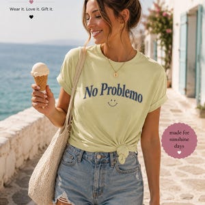 May include: A light yellow t-shirt with the words "No Problemo" in navy blue and a smiling face. The shirt is paired with denim shorts. The image also features a tote bag and an ice cream cone.