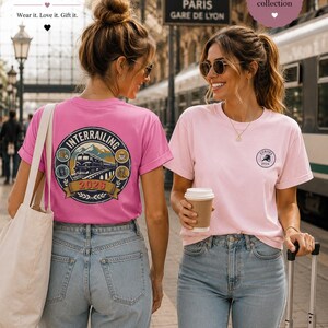 May include: A bright pink t-shirt featuring a large circular graphic on the back with a train, mountains, and the text 'INTERRAILING 2026'. A light pink t-shirt with a small circular 'EUROPE 2026' logo on the front chest. Both shirts are worn with blue jeans.