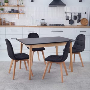 May include: A rectangular dining table with a matte black top and light wood legs, accompanied by four matching chairs featuring black upholstered seats with a tufted grid pattern and light wood legs, arranged in a kitchen setting.