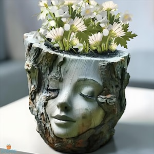 May include: A unique planter shaped like a tree stump with a serene face carved into the front. The planter is filled with white flowers and green foliage. The planter's exterior has a textured, weathered appearance.