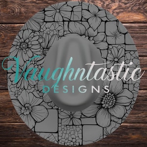 May include: A gray fedora-style hat with a floral design and the text "Vaughtastic DESIGNS". The hat features a gray crown and a wide brim decorated with black and white floral patterns.