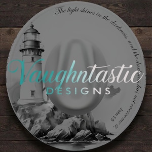 May include: A grey fedora hat featuring a black and white illustration of a lighthouse on a rocky shore. The text "Vaughntastic DESIGNS" is printed in the center, and the phrase "The light shines in the darkness, and the darkness has not overcome it. John 1:5" is printed along the brim.