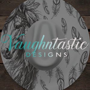 May include: A grey cowboy hat with a horse head and feather pattern. The hat has the text "Vaughtntastic DESIGNS" in a teal and white gradient. The background is a wooden surface.