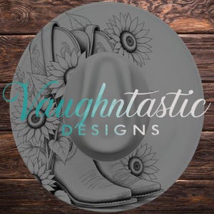 Puede incluir: Un sombrero gris redondo con una ilustración de línea negra de dos botas vaqueras rodeadas de girasoles. El texto "Vaughntastic DESIGNS" está impreso en una fuente azul claro y blanca en el centro del sombrero.