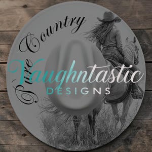 Könnte beinhalten: Ein grauer Cowboyhut mit einem Design, das eine Frau auf einem Pferd zeigt. Der Hut trägt den Text "Luxe Country Vaughtnastic DESIGNS" in schwarzer und türkisfarbener Schrift. Der Hintergrund ist eine Holzoberfläche.