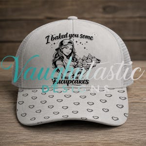 May include: A light gray trucker hat featuring a black graphic print of a person holding a tray of cupcakes. The text reads I baked you some Fucupcakes. The brim is decorated with a repeating pattern of small black heart outlines on a light gray background.