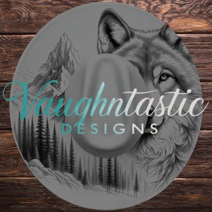 May include: Gray fedora hat with a detailed wolf and mountain landscape design. The hat features the text "Vaughtntastic DESIGNS" in a teal and white gradient. The hat's brim is visible.