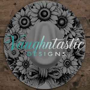 May include: A round, grey hat featuring a black and white line art pattern of sunflowers and a decorative bow. The text "Vaughntastic DESIGNS" is printed in a teal and white script and sans-serif font across the centre of the hat crown.