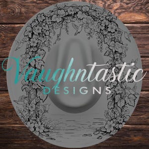 May include: A grey wide-brimmed hat featuring a black line art illustration of an arched trellis covered in flowers, leaves, and hummingbirds. The text Vaughtastic DESIGNS is printed in a teal and white script and block font across the center.