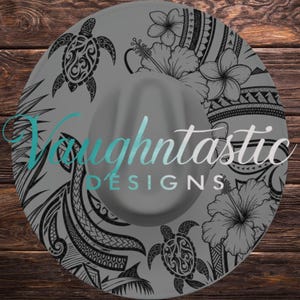 May include: Gray fedora hat with black tribal turtle, floral, and geometric designs. The hat features the text "Vaughtntastic DESIGNS" in a teal script. The hat has a wide brim and a rounded crown.