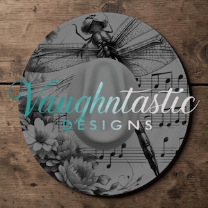 May include: A gray hat with a decorative brim featuring a dragonfly, musical notes, and floral elements. The hat has the text "Vaughntastic DESIGNS" in a teal and white gradient.