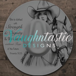 May include: Round decorative plate featuring a detailed illustration of a woman in a cowboy hat with a horse. The plate has text that reads "She is clothed with Strength & Dignity & She Laurns without Fear of the Future Proverbs 31:25" and "aughtntastic DESIGNS".