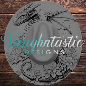 Könnte beinhalten: Ein grauer Hut mit breiter Krempe und einer schwarzen Strichzeichnung eines Drachen, umgeben von floralen Elementen. Der Text Vaughtastic DESIGNS ist in einer türkisfarbenen und weißen Schreib- und serifenlosen Schrift mittig aufgedruckt.