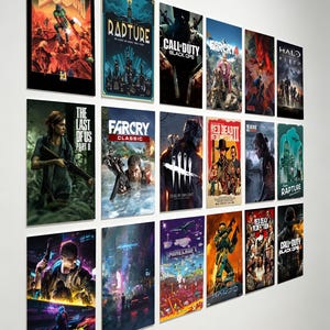 May include: A collection of framed video game posters, including titles like "DOOM," "Call of Duty," "Far Cry," and "Cyberpunk." The posters feature vibrant artwork and game titles, mounted on a white wall. The posters are rectangular and vary in size.