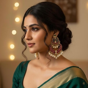 Puede incluir: Una mujer con un sari verde oscuro con ribete dorado y pendientes grandes y ornamentados. Los pendientes son rojos, verdes y dorados con detalles de perlas. La mujer tiene el pelo oscuro recogido en un moño.