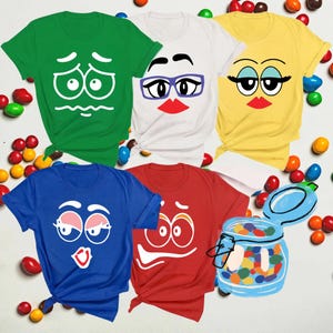 May include: Five short-sleeved t-shirts in green, white, yellow, blue, and red, each featuring a unique cartoon face graphic. The white shirt includes purple glasses. A blue line-art illustration of a glass jar filled with colorful candies is positioned in the bottom right corner.