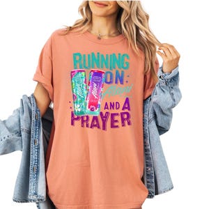 A woman wearing a pink t-shirt with a graphic design and text, standing against a white background.