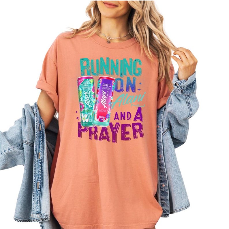 A woman wearing a pink t-shirt with a graphic design and text, standing against a white background.