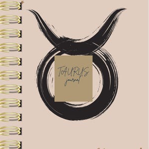 May include: A spiral-bound journal with a light beige cover featuring a black brushstroke Taurus zodiac symbol. A tan rectangular box in the center displays the text TAURUS journal in black. The cover is decorated with small gold star accents.