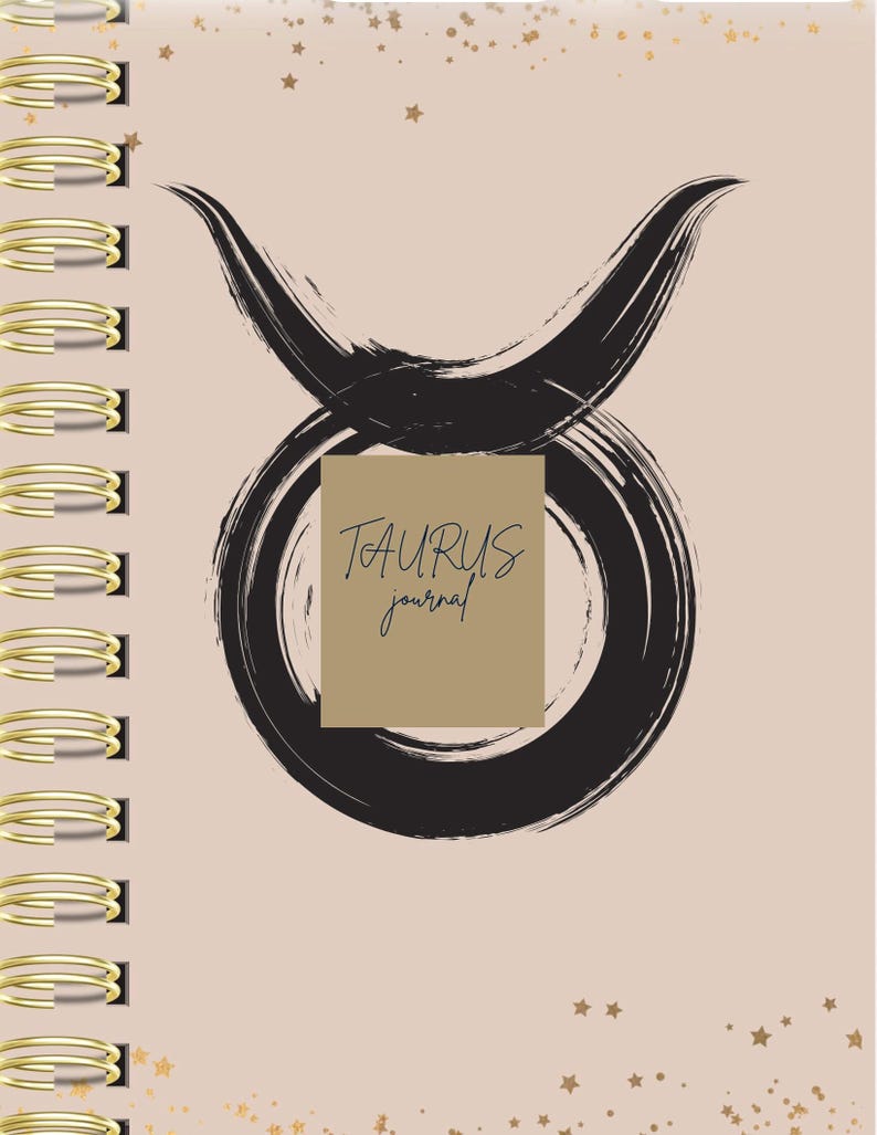 May include: A spiral-bound journal with a light beige cover featuring a black brushstroke Taurus zodiac symbol. A tan rectangular box in the center displays the text TAURUS journal in black. The cover is decorated with small gold star accents.