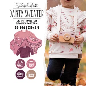 May include: A sewing pattern for a Dainty Sweater by Schleiferwerk, sizes 56-146, in German and English. The image displays three variations of the sweater in shades of pink and floral patterns, alongside a child wearing a floral sweater.
