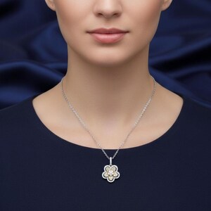 Puede incluir: Un collar de plata con un colgante de flor. El colgante presenta un grupo central de peque&ntilde;as piedras redondas de tono amarillo rodeadas de piedras blancas, creando un dise&ntilde;o floral. El collar se lleva sobre un fondo azul oscuro.