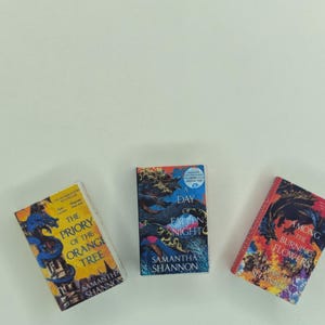 May include: Three books with vibrant covers are shown. The titles are "The Priory of the Orange Tree", "A Day of Fallen Night", and "Among the Burning Flowers". The author's name, Samantha Shannon, is printed on each book.