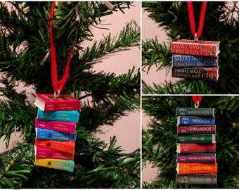 May include: A set of three miniature book ornaments hanging from red ribbons. One ornament features a stack of colorful A Court of Thorns and Roses books, another shows Crescent City titles, and the third displays the Throne of Glass series.