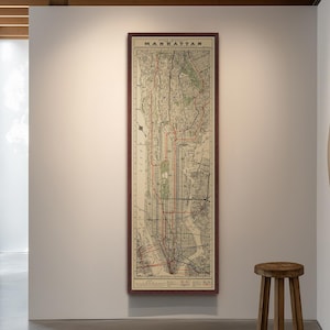 May include: A framed vintage map of Manhattan, New York City, with a dark wood frame. The map features red and black lines indicating roads and transit routes. A small wooden stool sits in front of the map.