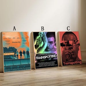 Può includere: Sono esposti tre poster incorniciati del film "Trainspotting". I poster hanno diverse combinazioni di colori e design, con il titolo del film in evidenza. Un poster ha il testo "Choose life."
