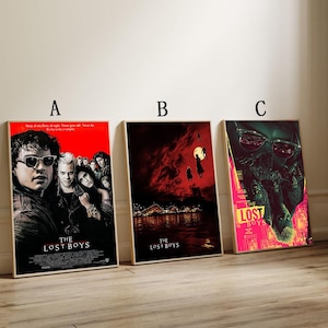 May include: Three framed movie posters for "The Lost Boys" are displayed. The posters feature different scenes and color schemes, including a red background with the movie title. The posters are in wooden frames.