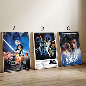 May include: Three framed Star Wars film posters. The posters showcase iconic characters and scenes from the original trilogy. The posters are titled "Return of the Jedi", "Star Wars", and "The Empire Strikes Back". The posters are in a light wood frame.