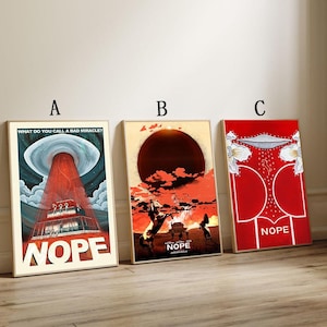 以下が含まれることがあります： 「NOPE」の文字が入った3つの額入り映画ポスター。ポスターはヴィンテージスタイルで、赤、白、ベージュの色使いです。1つのポスターにはUFOと赤い光線が描かれています。