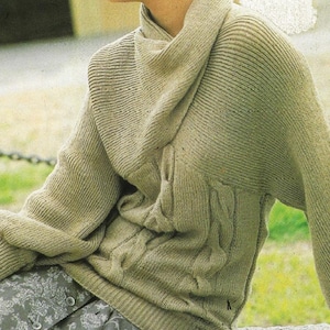 May include: A light olive green knit sweater with a high, draped neckline. The sweater features ribbed and cable knit detailing. The sleeves are long, and the overall style is relaxed and comfortable. The sweater is paired with a patterned garment.