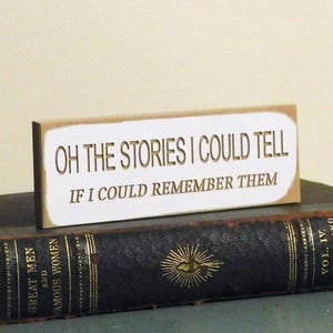 May include: A white wooden sign with the text "Oh the stories I could tell if I could remember them".