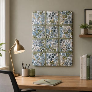May include: A rectangular fabric-covered memo board featuring a floral pattern in shades of blue, green, and white. The board is divided into a grid by olive green ribbons secured with small metal buttons at each intersection point.