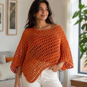 Puede incluir: Un top de ganchillo color naranja quemado que presenta un patrón de malla abierta y ancha con una silueta holgada y cuadrada, un escote barco ancho y mangas tres cuartos, usado sobre una capa base naranja sólida con pantalones blancos.