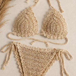 Könnte beinhalten: Ein beigefarbenes Häkel-Bikini-Set bestehend aus einem Triangel-Oberteil mit gewelltem Rand und einem passenden Unterteil zum Binden an den Seiten. Das Set ist aus strukturiertem Garn gefertigt und hat geflochtene Bänder mit kleinen Quasten.