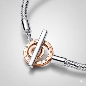 May include: A silver bracelet with a rose gold and silver clasp. The clasp features a circular design with the word "PANDORA" engraved around the edge. The bracelet has a textured, snake chain design.