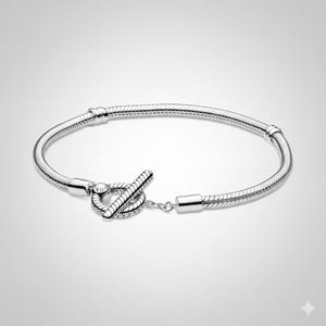 May include: A silver bracelet with a snake chain design. The bracelet features a toggle clasp closure. The bracelet is a simple, elegant piece of jewelry.