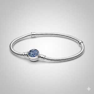 以下が含まれることがあります： 小さな青い宝石で飾られた丸い留め金が付いたシルバーブレスレット。ブレスレットはスネークチェーンのデザインで、留め金で固定されています。全体的なデザインはエレガントで、普段使いに適しています。長さは約18cmです。