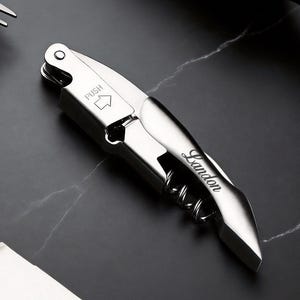 May include: A stainless steel wine opener with a corkscrew and a lever. The opener has the word "Push" with an arrow and the name "Landon" engraved on the side. The opener is on a black marble surface.