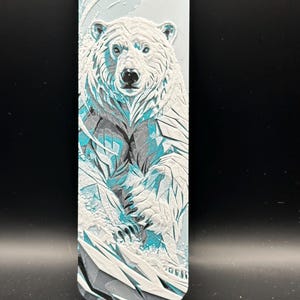 May include: A rectangular bookmark featuring a three-dimensional relief of a polar bear. The design is rendered in shades of white, light blue, and dark gray, depicting the bear amidst icy, jagged textures with a smooth, rounded top edge.