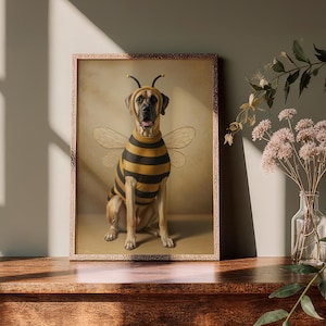Könnte beinhalten: Ein gerahmter Druck, der einen Hund in einem Bienenkostüm zeigt. Der Hund trägt ein schwarz-gelb gestreiftes Outfit mit Flügeln und Antennen. Das Kunstwerk hat einen Vintage-Stil und wird auf einer Holzoberfläche präsentiert.