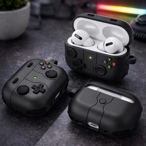 Könnte beinhalten: Schwarze Schutzhüllen für kabellose Ohrhörer, im Design von Spielecontrollern. Eine Hülle ist geöffnet und zeigt weiße Ohrhörer. Die Hüllen verfügen über Knöpfe, Steuerkreuze und die Buchstaben A, B, X und Y in verschiedenen Farben.