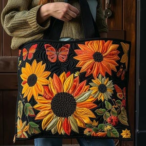 Könnte beinhalten: Schwarze Tragetasche mit einem gesteppten Sonnenblumen- und Schmetterlingsdesign. Die Tasche zeigt große, lebendige Sonnenblumen in Gelb-, Orange- und Rottönen mit detaillierten Nähten. Schmetterlinge in ähnlichen Farben sind ebenfalls abgebildet.